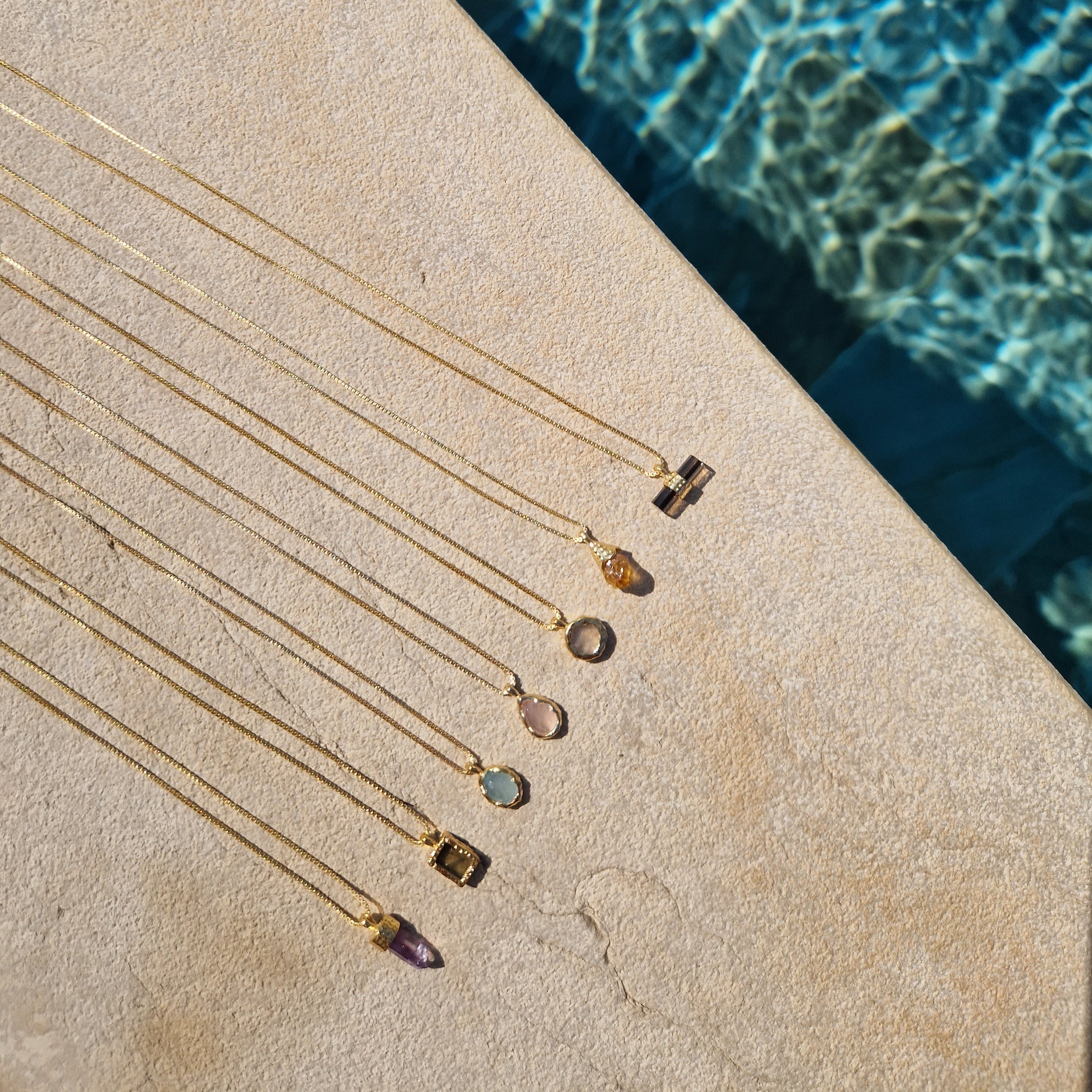 Crystal healing necklaces on a stone surface next to a pool.
