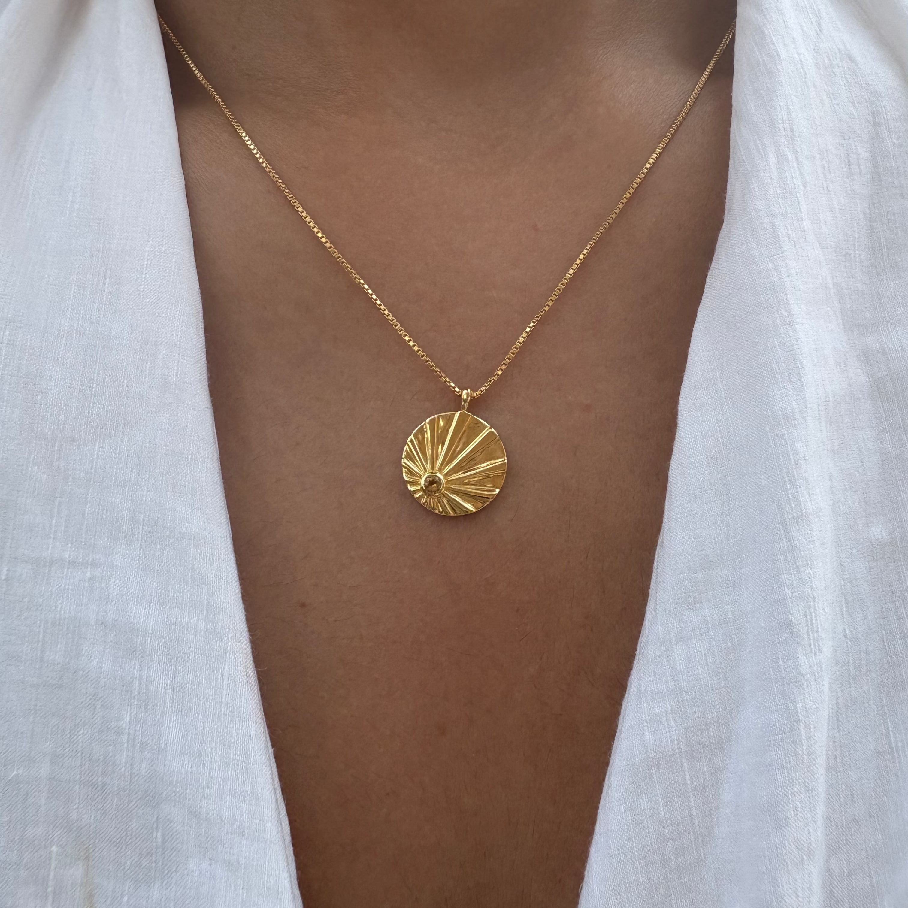 Gold sun necklace with a circular citrine pendant worn by a person in a white shirt.