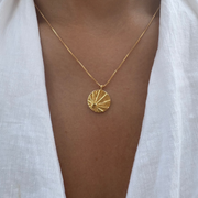Gold sun necklace with a circular citrine pendant worn by a person in a white shirt.