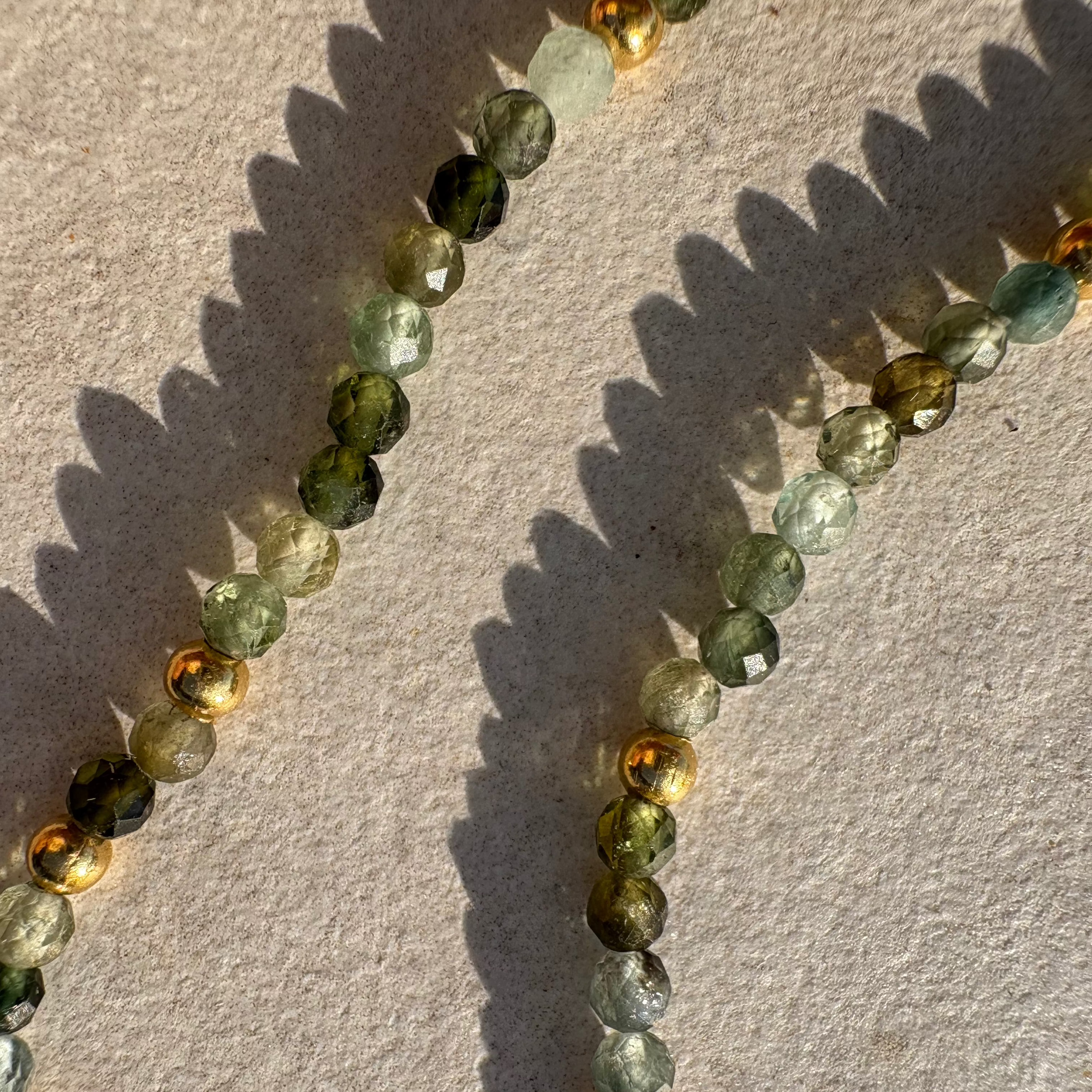 Necklace with green tourmaline and gold beads on a textured beige surface