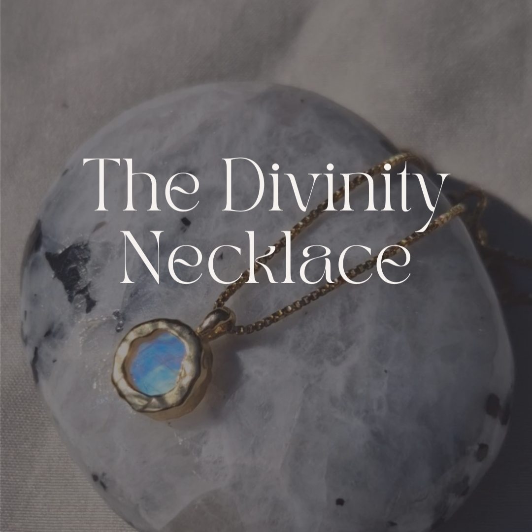 Necklace with a blue stone pendant on a gray stone surface, labeled 'The Divinity Necklace'.