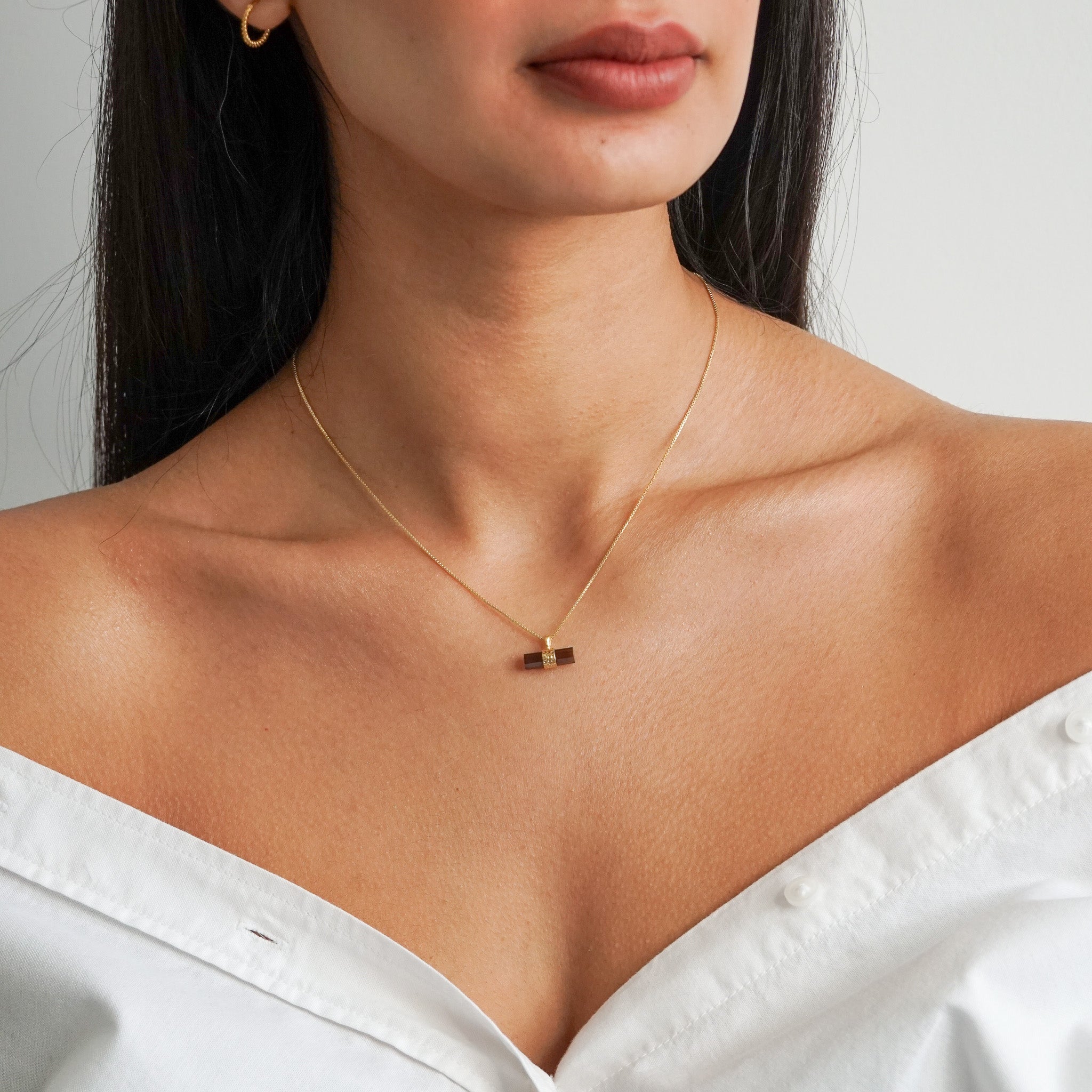 Dark brown smoky quartz pendant in a bar shape with a gold box chain on a models neck