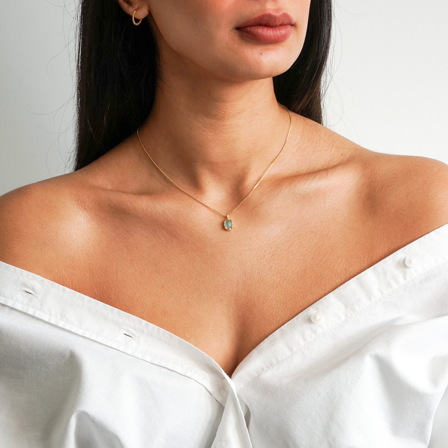 Aqua green oval aquamarine pendant with irregular faceting on an 18k gold vermeil box chain on model neck